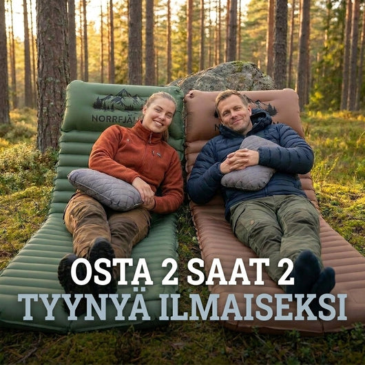 Pariskunta lepää vihreällä ja ruskealla Ilmapatja PRO V2:lla harmaiden tyynyjen kanssa mäntymetsässä, tarjousteksti ilmaisista tyynyistä