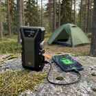 Vevradio lader en mobiltelefon via USB-kabel på en sten ved teltet, mobilskærmen viser et ladesymbol