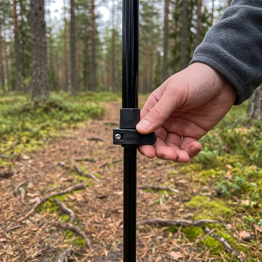 Tommelfinger lukker hurtiglåsen på en vandringsstav, skovsti i baggrunden