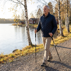 Ældre mand går med vandrestave på en grusvej ved en sø en høstmorgen