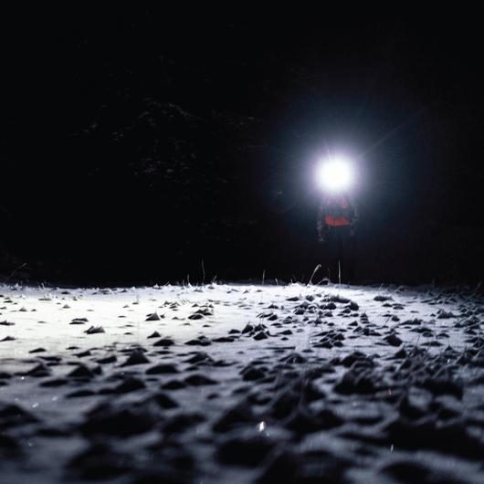 Otsalampun valkoinen valo valaisee huurteista ja lumista maata yön pimeydessä